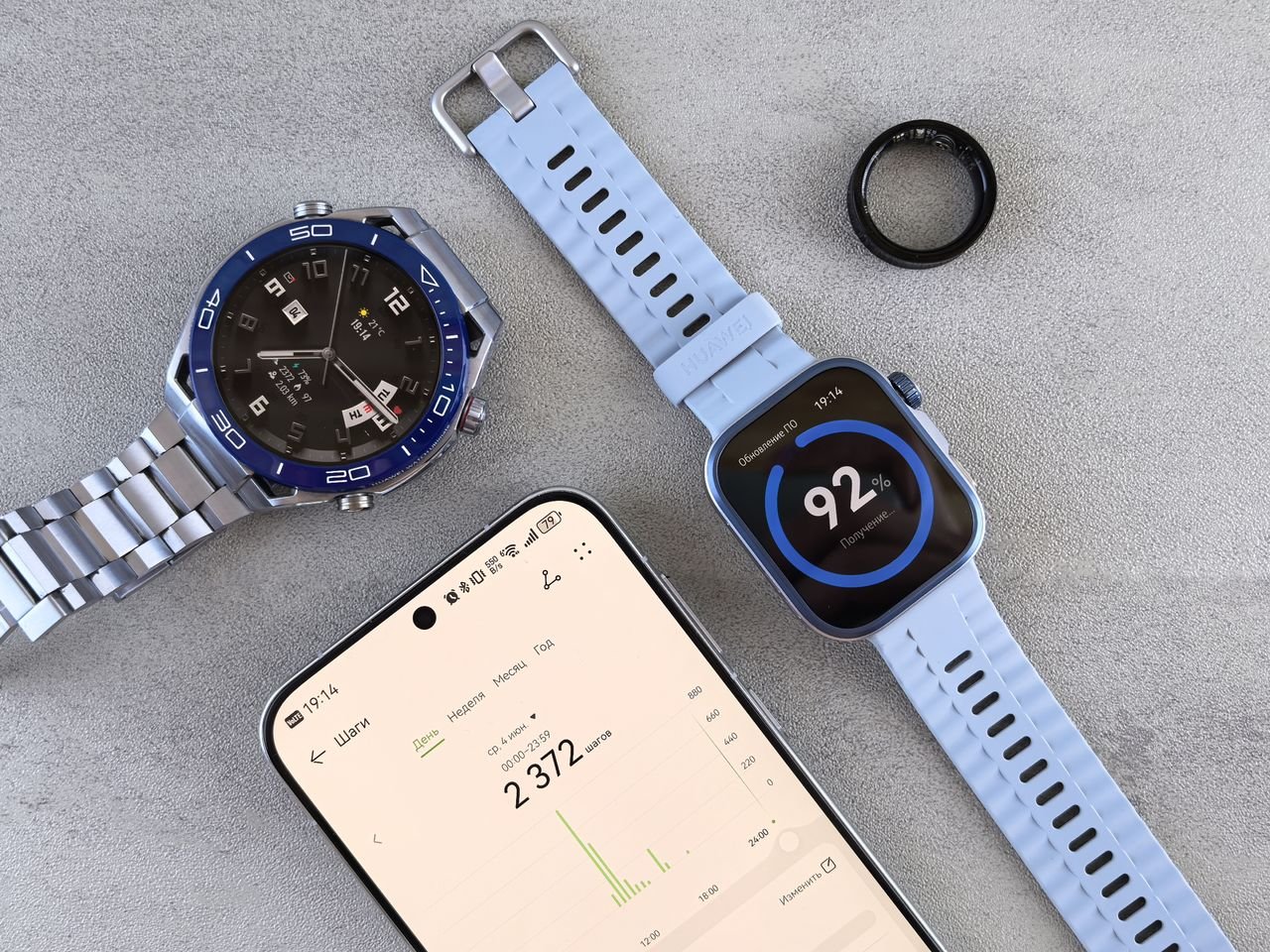 Smartwatch, ring tracker, and smartphone displaying fitness data on a gray surface.
